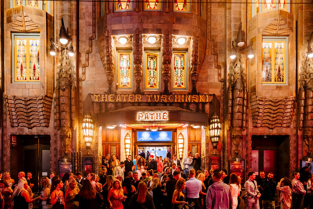 Guests arrive under the lit marquee of a theatre on the night of an award show.