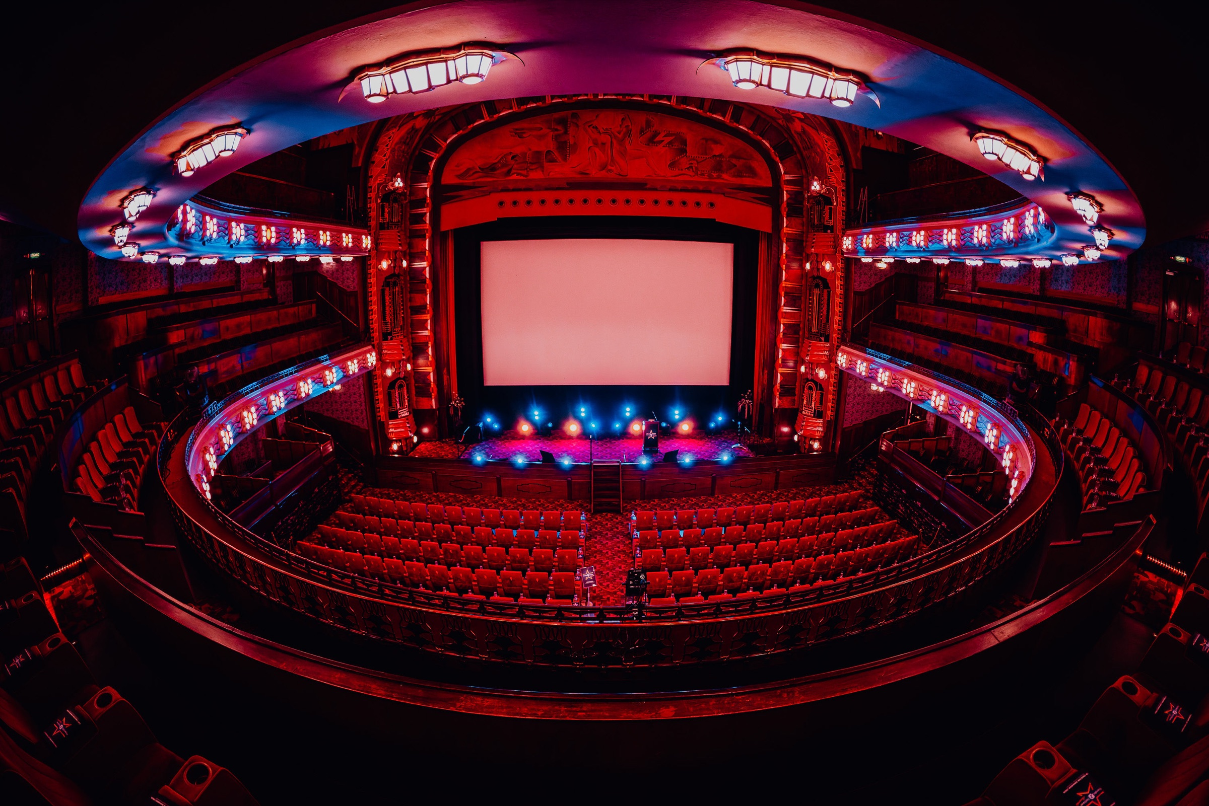 An empty theatre auditorium before doors open, red seats and a lit stage.