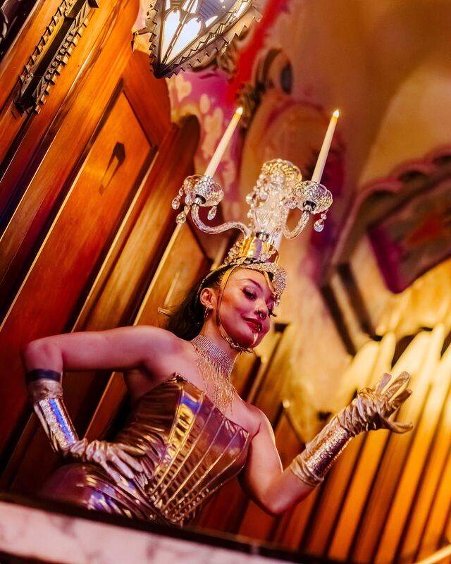 A performer in a gold costume with a candelabra headpiece poses in the art deco lobby of Theater Tuschinski