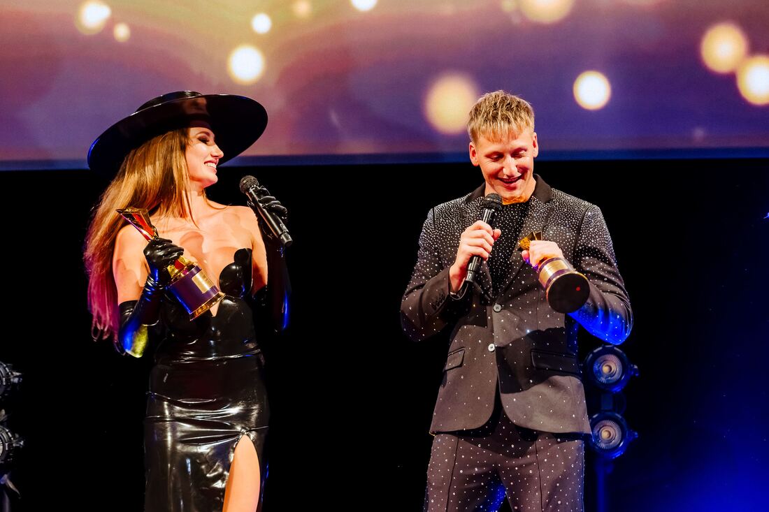 A winner with the trophy and a presenter with a microphone on stage at the F2F Creator Awards 2026, gold light behind them