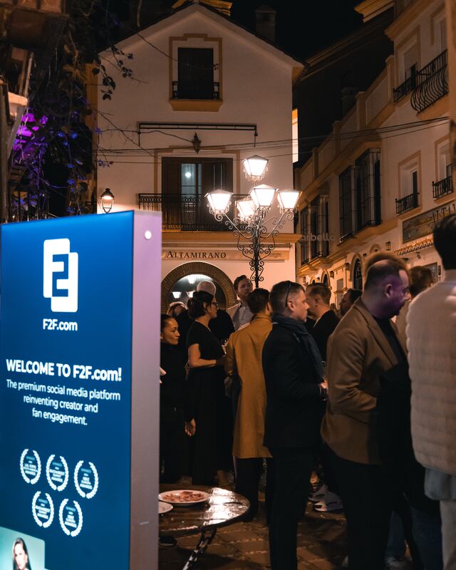 Guests arrive at a dinner on a lit street at night, next to a welcome banner of the host company
