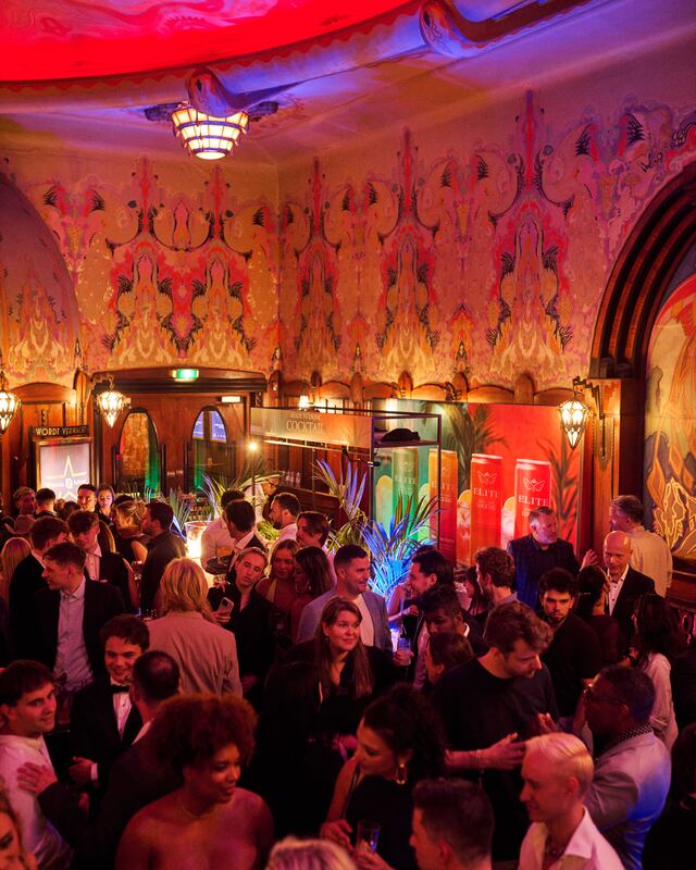 Guests with drinks fill the art deco lobby of Theater Tuschinski before the show, under the painted ceiling