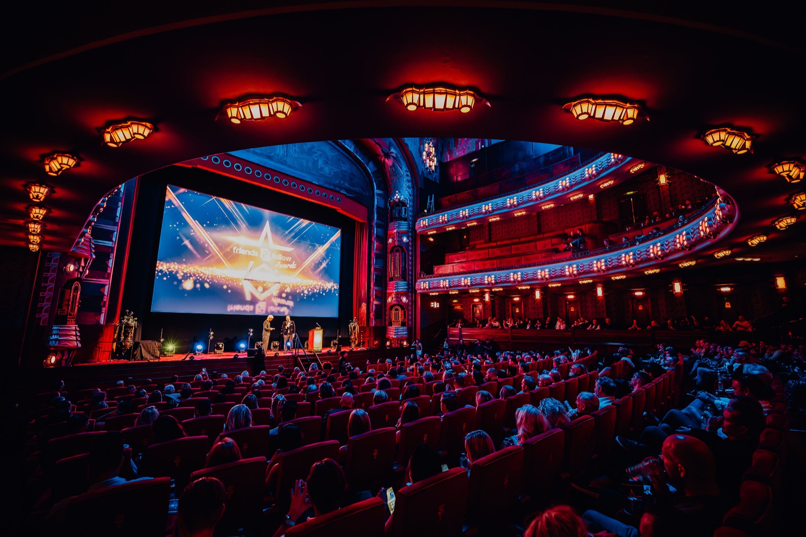 A full theatre on the night of an award show, guests in evening wear in red seats.